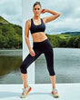 Women's three-quarter performance pocket leggings in black, featuring an elasticated waistband and side pockets against a scenic outdoor background.