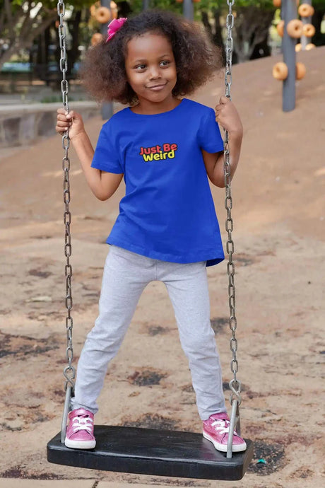 Kid wearing Just Be Weird Kids Softstyle T-Shirt on swing, outdoor playground.