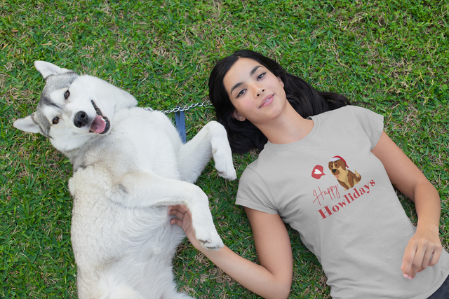 Women's t-shirt with "Happy Howlidays" design and dog, worn by woman lying on grass.